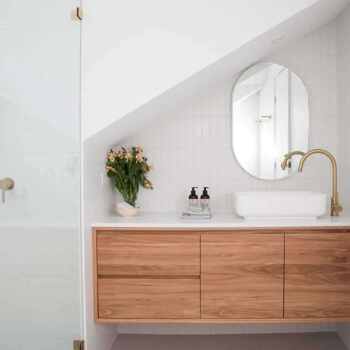 A bright, minimalist bathroom featuring brushed brass fixtures, including a gooseneck faucet and a shower rail system.