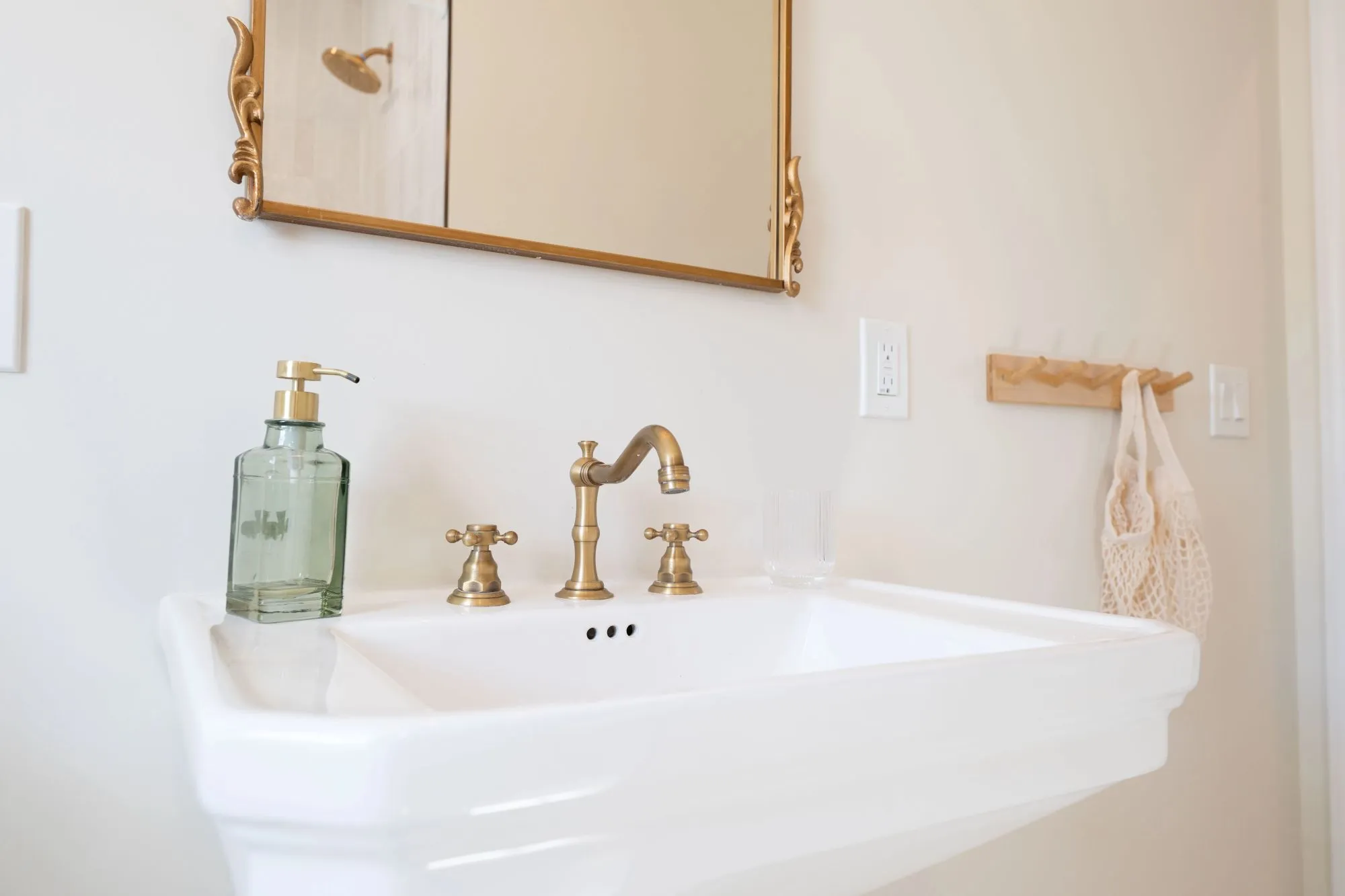 A traditional white pedestal basin featuring a three-hole faucet set in a brushed brass finish. 