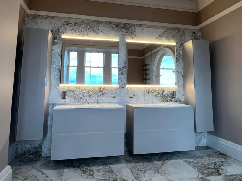 Modern luxury bathroom with marble-effect floor-to-ceiling tiles, a double floating vanity set, and two LED-backlit mirrors framed by tall grey storage cabinets.