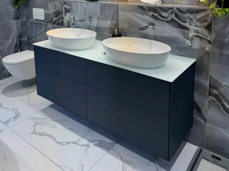 Modern luxury bathroom with dark marble-effect wall tiles, a navy double vanity with vessel sinks, and a large wide-format backlit mirror.