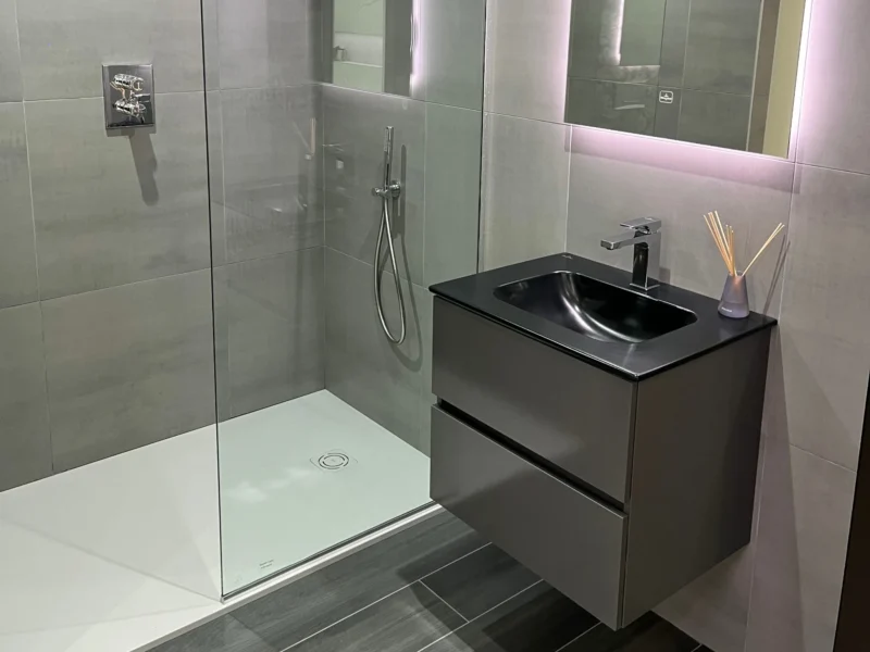 A modern bathroom with grey tiles, a black integrated sink on a dark grey vanity, and a walk-in shower.
