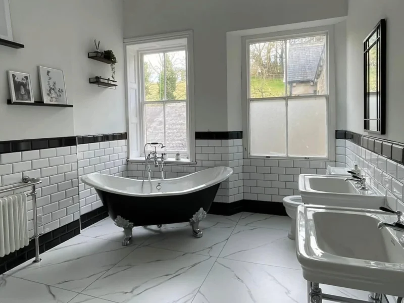 A black and white, claw-footed free-standing bathtub in a monochromatic, tiled bathroom.