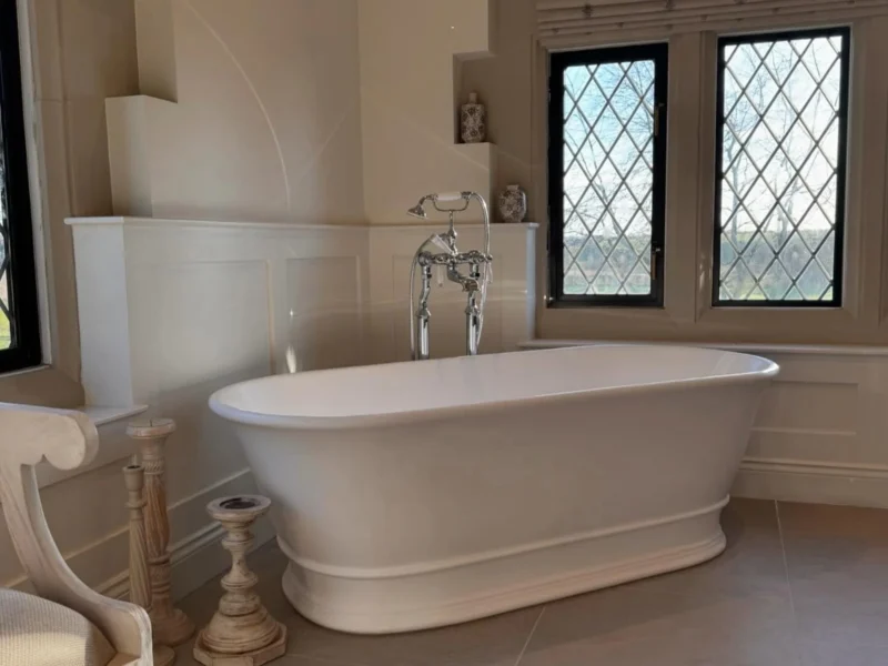 A white freestanding bath in a bathroom with a neutral colour scheme and cross-barred windows.