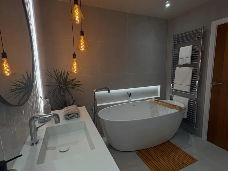 A large, ovular freestanding bath in a minimalist bathroom featuring a rattan bathmat and hanging lights.