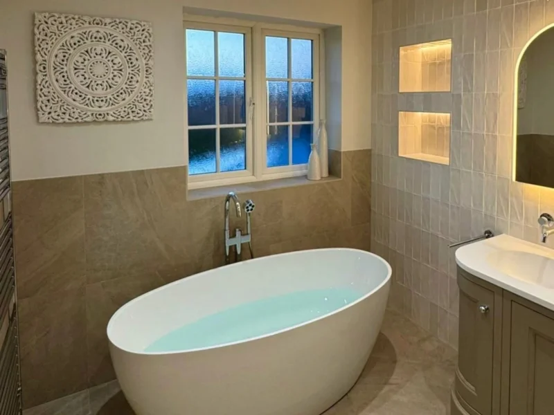 A large, ovular freestanding bathtub in a bathroom with olive cabinetry and natural stone finishes.