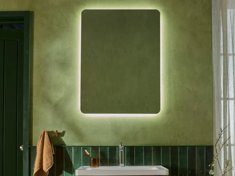 A square, soft-cornered LED vanity mirror hung on a mossy green bathroom wall above a white sink.