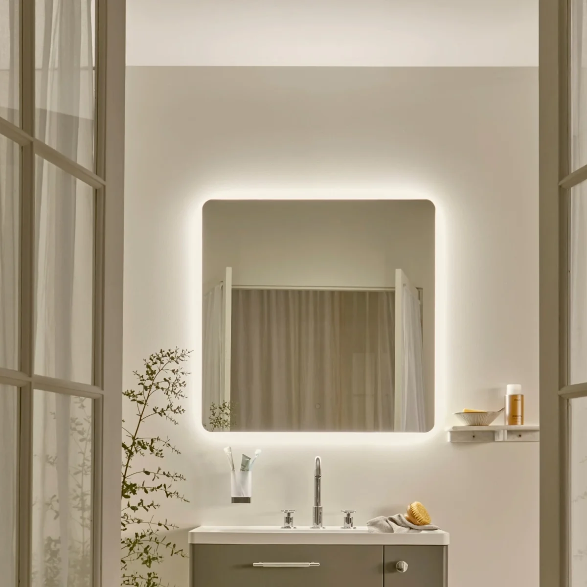 Two open doors leading into an off-white coloured bathroom, with a square vanity mirror above the sink.