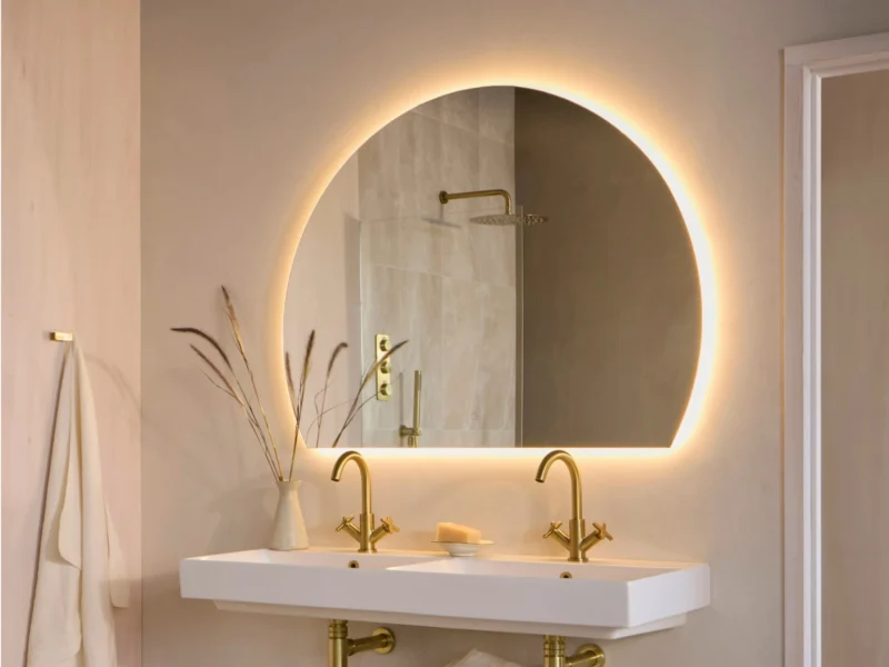 An LED vanity mirror hung on a blossom pink wall, above a white, floating sink.