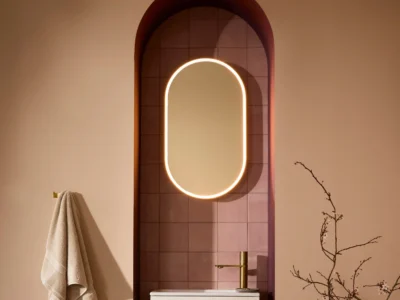 An oval-shaped LED vanity mirror in a nook in a rose pink bathroom wall.