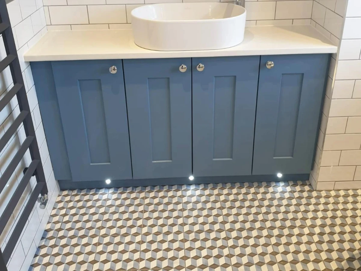 A bathroom vanity unit with four blue doors, built-in lighting, and a large round sink and geometric tiles on the floor.