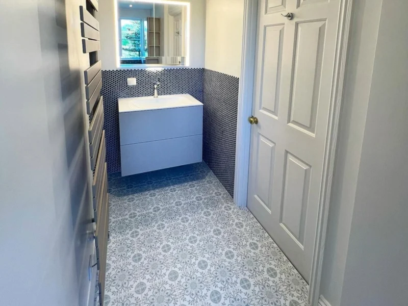 A small bathroom with a floating vanity unit, backlit mirrored cabinet, and blue and white tiling on the floors and wall. 