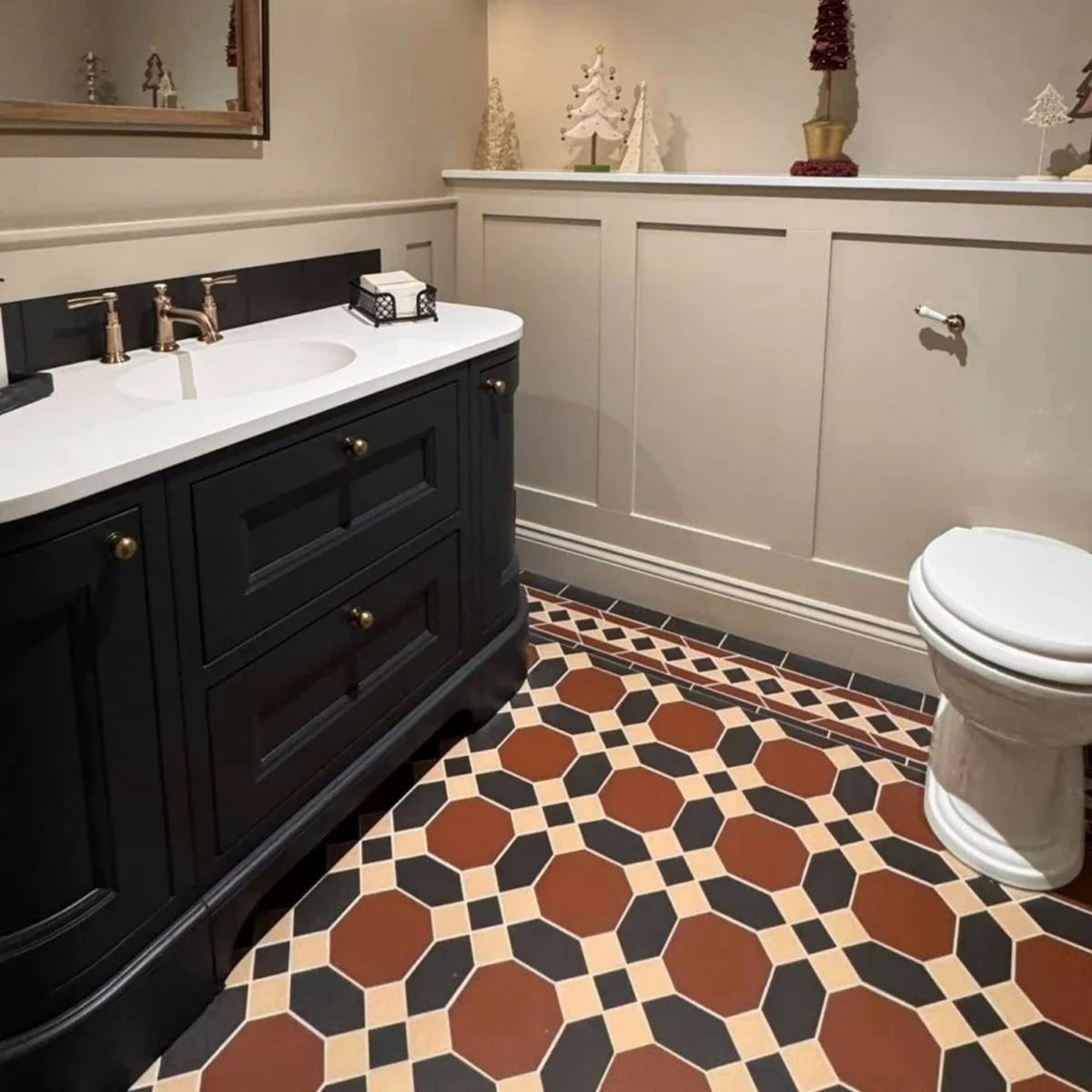 A traditional bathroom with a large black vanity, wall panelling, and decorative floor tiles in cream, red, and navy.