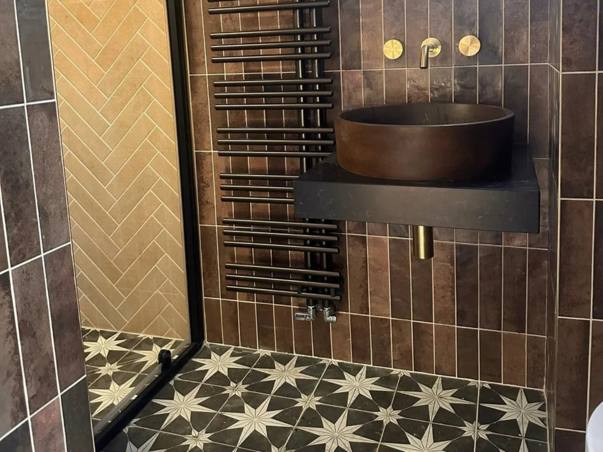 A rustic bathroom with a walk-in shower, wall-mounted sink, and dark brown colour palette with decorative star-shaped floor tiles.