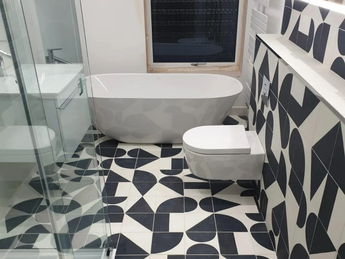 A modern bathroom with a glass shower cubicle and white freestanding bath and rounded, geometric floor and wall tiles.