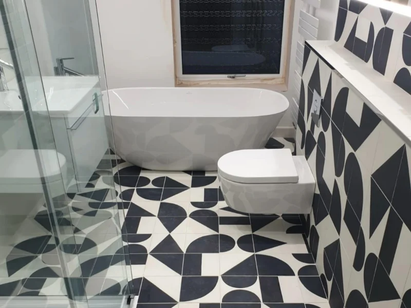 A modern bathroom with a glass shower cubicle and white freestanding bath and rounded, geometric floor and wall tiles. 