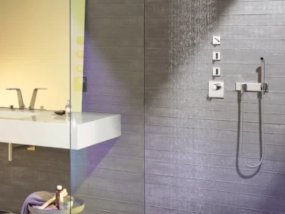 A Dornbracht shower and bathroom. The wall is grey and there are silver finishes on the tap and shower pieces.