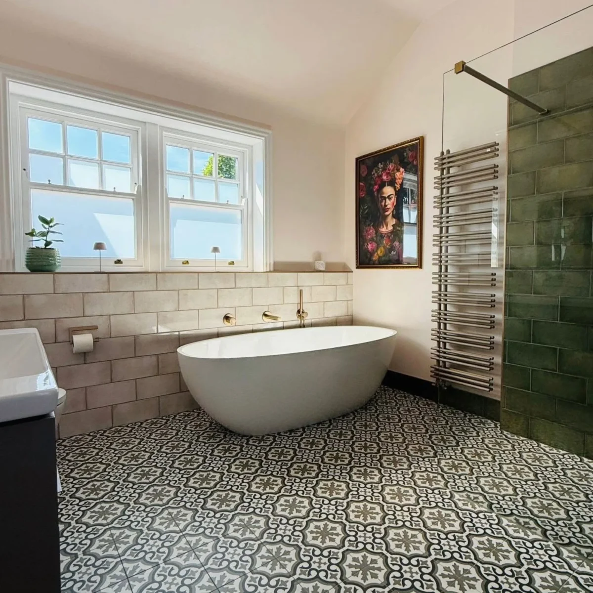 Luxurious modern bathroom featuring a white freestanding bathtub, patterned floor tiles, green tiled walk-in shower, and a framed portrait on the wall.